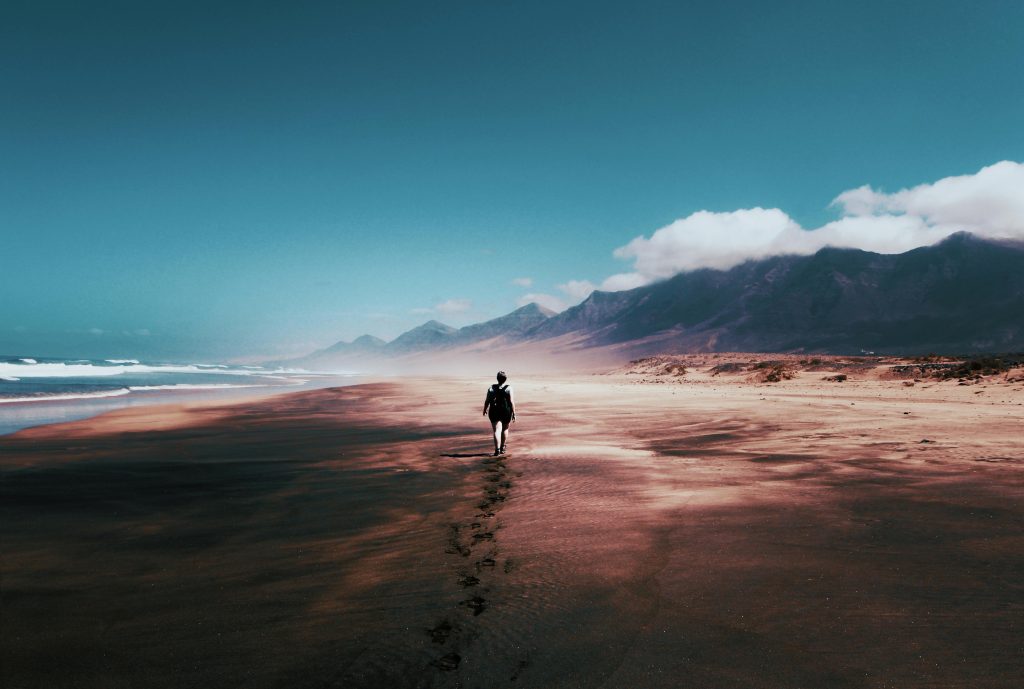 A person walking away on a beach towards the horizon.