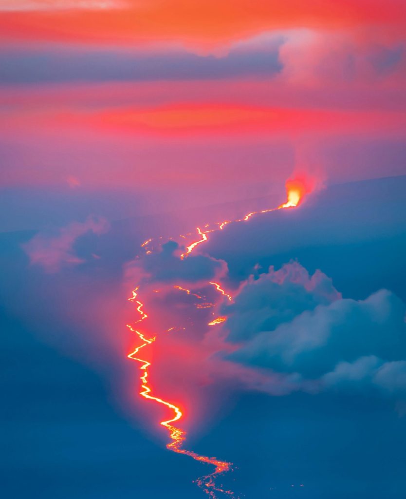 Colorful photo of lava from a far off volcano creating a stream through dark countryside.