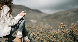 Woman belonging with nature as she sits on a rock with coffee cup surrounded by sagebrush and beautiful scenery.