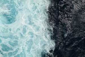 Deep ocean with clear boundary between dark blue calm water and light blue and white churning water.
