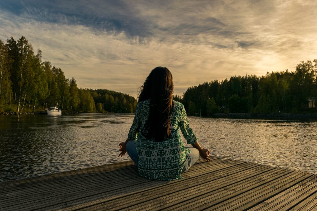 Woman practicing the art of living in the present while sitting by a lake