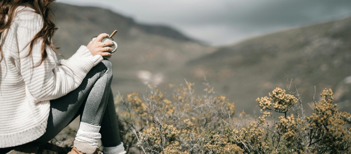 Woman belonging with nature as she sits on a rock with coffee cup surrounded by sagebrush and beautiful scenery.