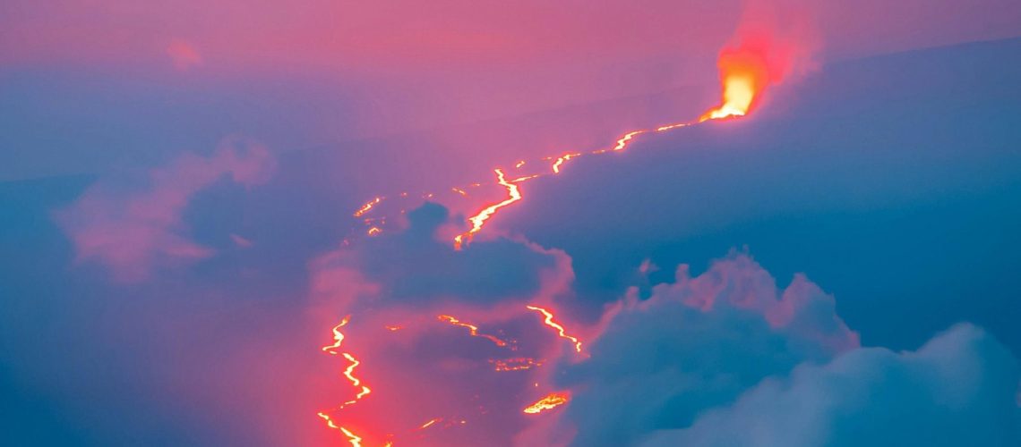 Colorful photo of lava from a far off volcano creating a stream through dark countryside.