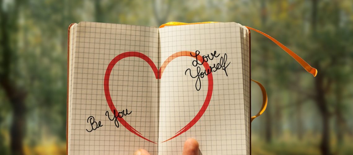 Forest background with outheld journal and written text of "Be you," and "Love yourself."