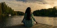 Woman practicing the art of living in the present while sitting by a lake