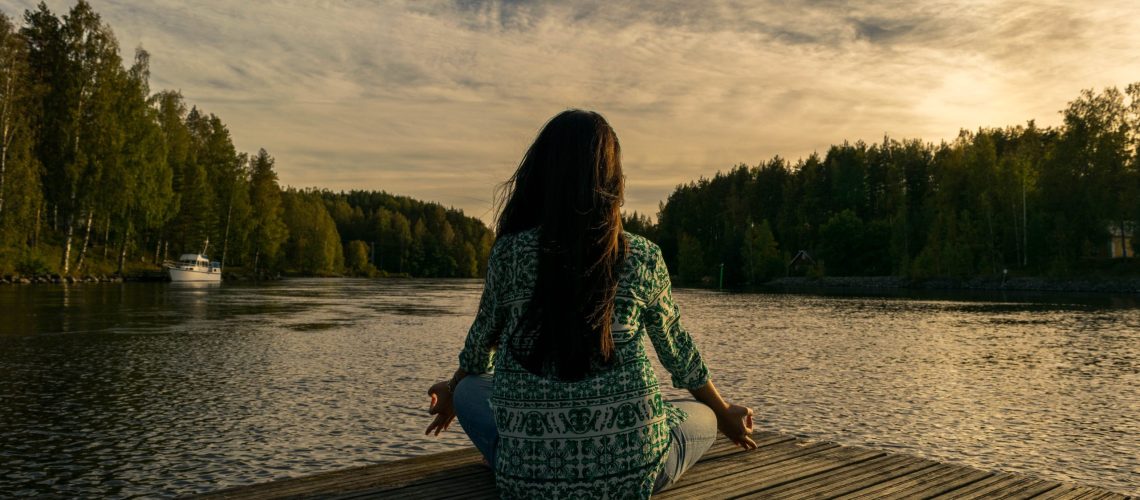 Woman practicing the art of living in the present while sitting by a lake